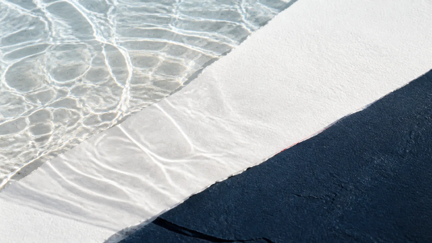 Klare Wasserreflexe über mineralweißem Papier und einer tiefblauen Steinfläche.